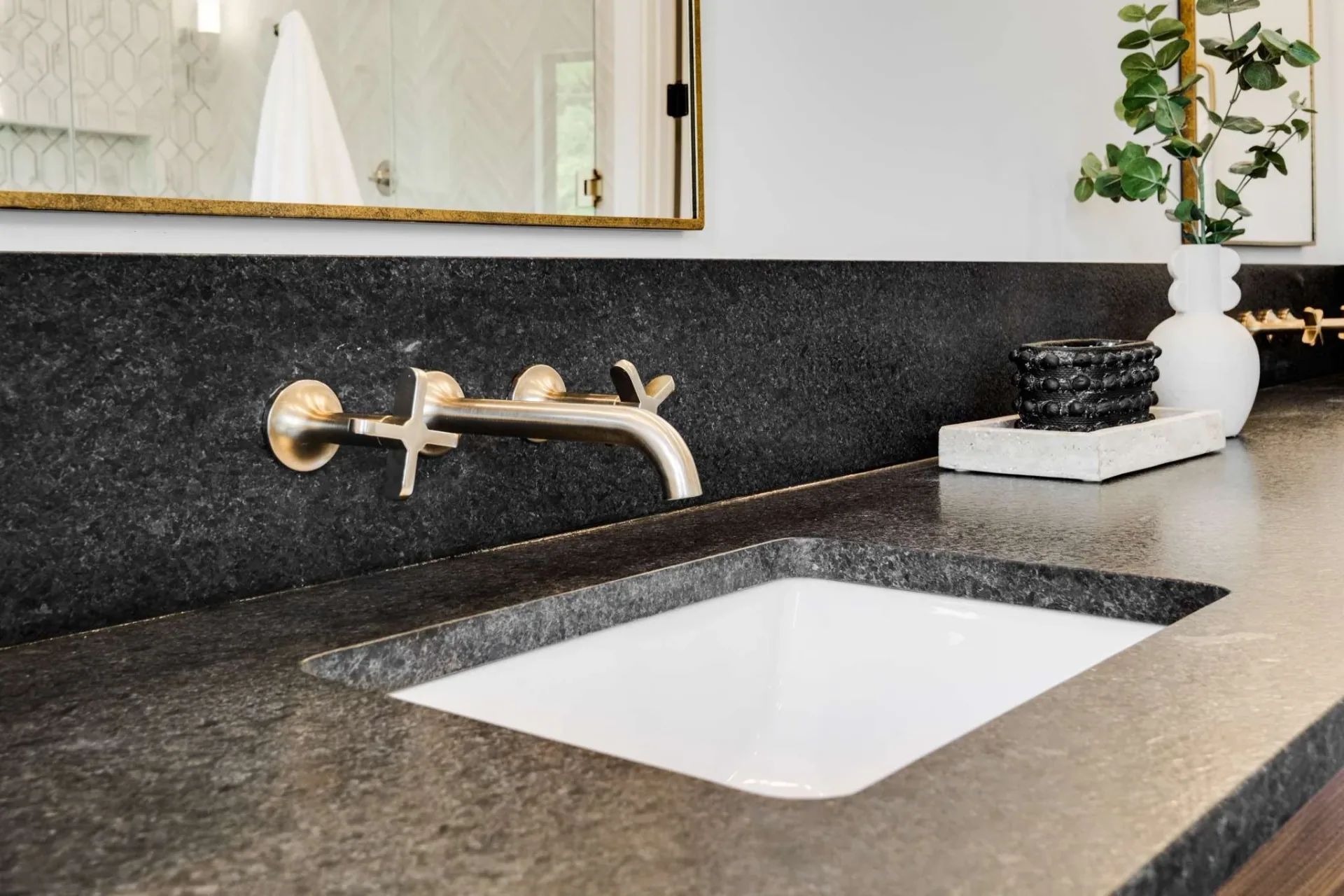 Wall mounted faucet above a wood vanity and dark countertop