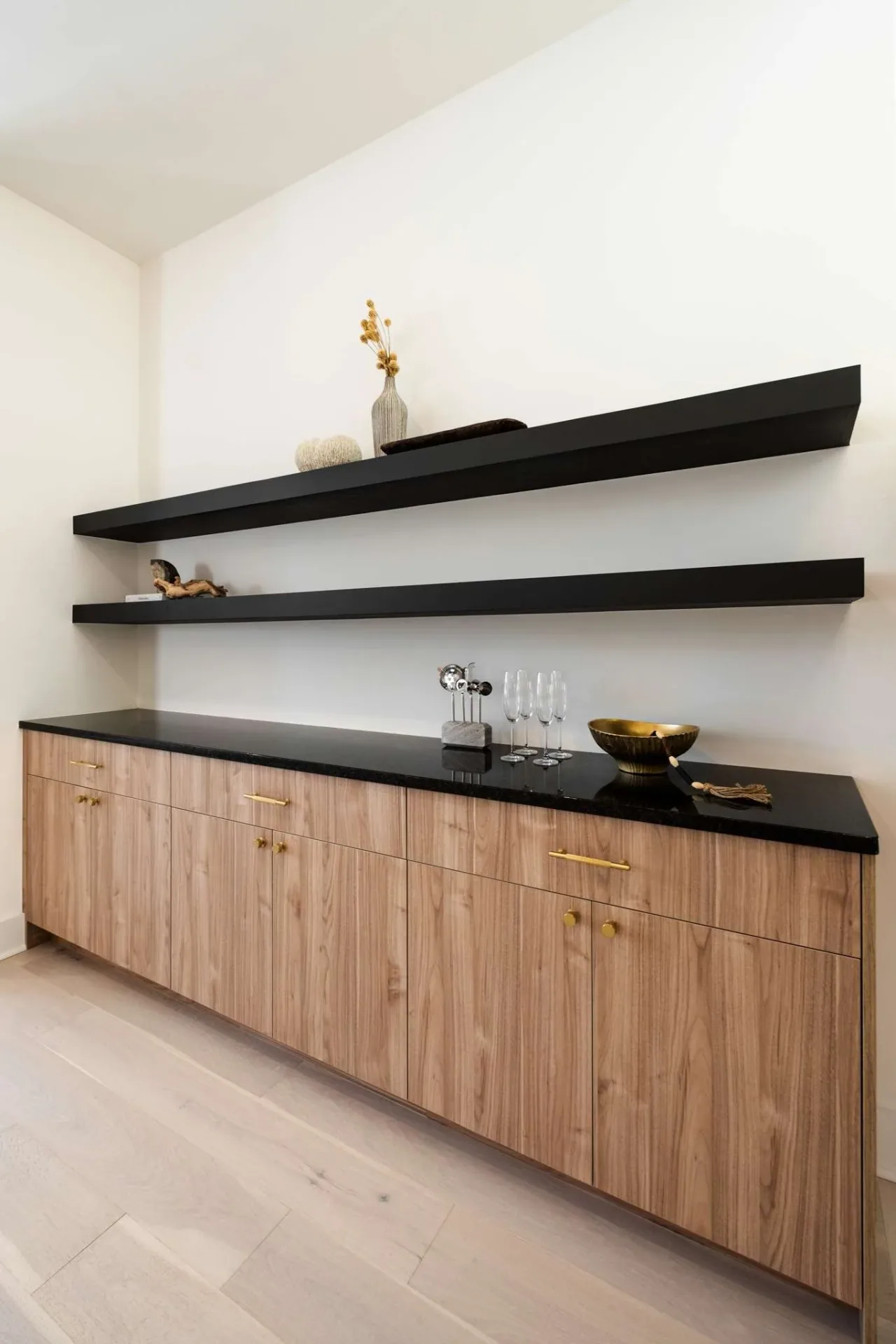 Low wood bar cabinetry beneath two dark shelves