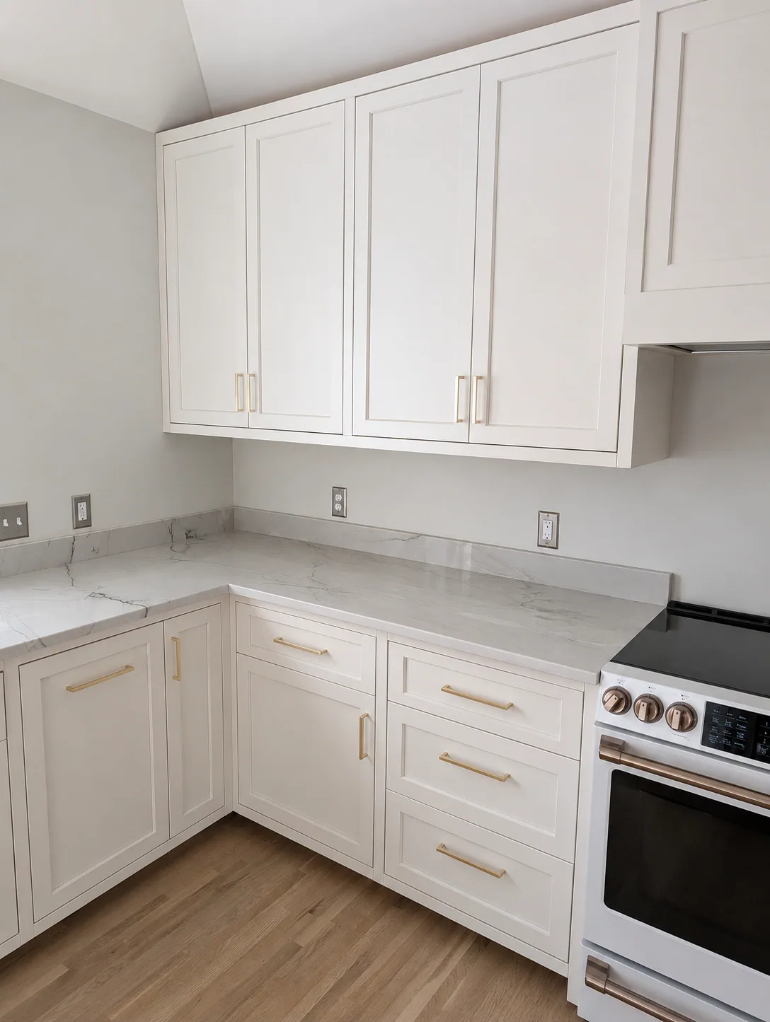 Miller Kitchen corner cabinetry with brass pulls, pale veined counters, and a white range